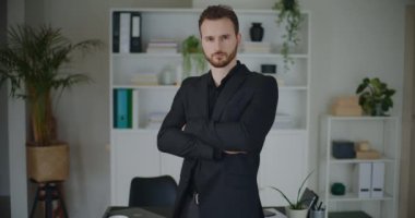 İş yerinde siyah iş kıyafetleri içinde kollarını kavuşturmuş kendine güvenen genç ve yakışıklı iş adamının portresi.