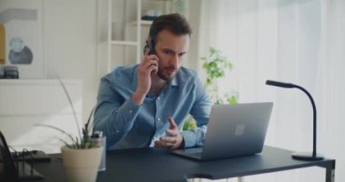 Ofiste dizüstü bilgisayarla otururken telefonla stratejiyi tartışan yakışıklı genç bir işadamı.