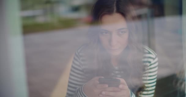 美しい若い女性がスマートフォンでソーシャルメディアを閲覧しながら 窓から見た自宅で夢を見る — ストック動画
