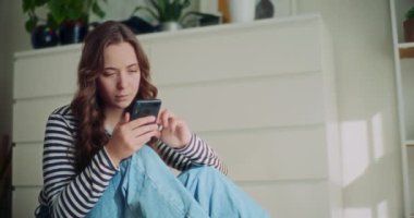 Evde oturma odasında otururken sosyal medyada akıllı telefondan gülümseyen güzel bir kadın.