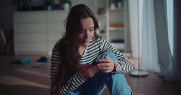 自宅のリビングルームの床に座っているスマートフォンを持つ孤独な女性のロックダウンスローモーションショット — ストック動画