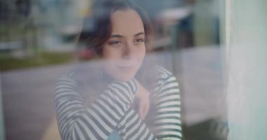 Gülümseyen güzel bir genç kadın hayal kuruyor. Pencereden görünen cep telefonunu kullanarak.