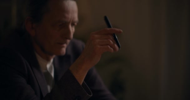 オフィスで深夜考えながらペンを保持している年配のビジネスマン — ストック動画