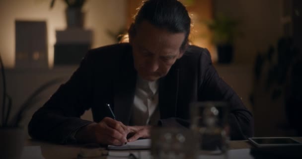 シニアビジネスマンは 職場で深夜勤務中に机で日記を書いています — ストック動画