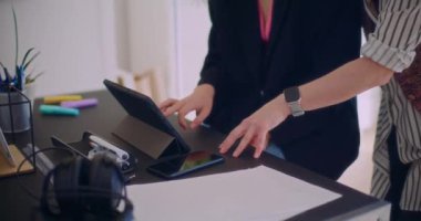 Şirket işyerindeki masada dijital tablet üzerinde konuşurken el kol hareketi yapan genç bayan meslektaşların orta bölümü