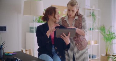 Genç iş kadınının dijital tablet tutarken birlikte çalıştığı kadın meslektaşına stratejiyi açıklarken yavaş çekim.