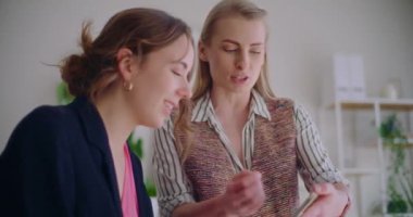 Genç iş kadınları şirket ofisinde çalışırken cep telefonuyla strateji tartışıyor