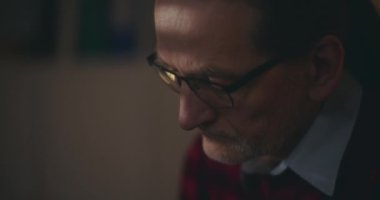 Düşünceli yaşlı adam loş bir evde, gecenin sessizliğinde hayat yolculuğuna ciddiyetle yansıyor.