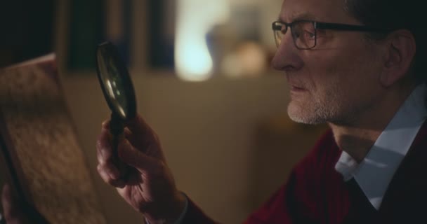 Ηλικιωμένος Κύριος Απορροφάται Στη Νυχτερινή Ανάγνωση Χρησιμοποιώντας Ένα Μεγεθυντικό Φακό — Αρχείο Βίντεο