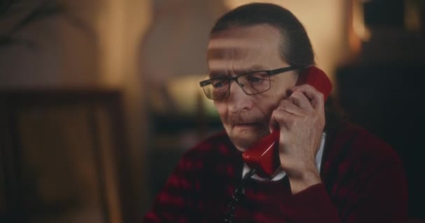 高齢の紳士が夜の静かな雰囲気の下でヴィンテージ電話でノスタルジックな会話をする — ストック動画