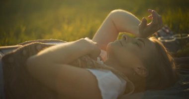 Gülümseyen bir kadının doğal güzelliğinin ortasında, rahat bir piknik battaniyesinde rahatlamaya alışması gibi boş zamanların esansını yakalayın.