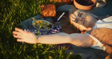 Gülümseyen bir kadının doğal güzelliğinin ortasında, rahat bir piknik battaniyesinde rahatlamaya alışması gibi boş zamanların esansını yakalayın.