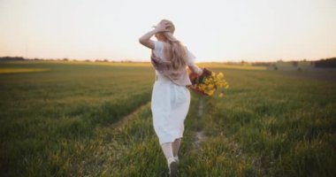 Canlı bir kadının, altın çiçeklerin arasında enerji ve canlılık yakalayan, resimli bir yağ tohumu tarlasında koşarken çekilmesi.