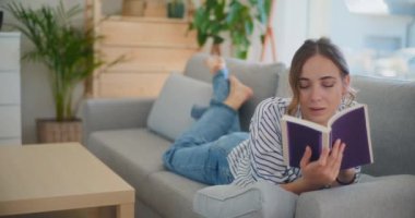 Oturma odasındaki bir kanepede oturmuş edebiyat dünyasına dalmış kitap okumaya dalmış odaklanmış ve düşünceli bir kadın.
