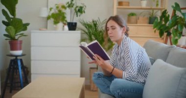 Oturma odasındaki bir kanepede oturmuş edebiyat dünyasına dalmış kitap okumaya dalmış odaklanmış ve düşünceli bir kadın.
