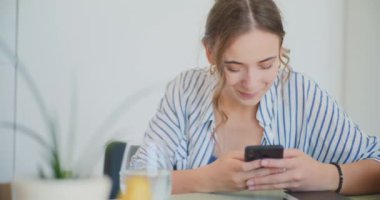 Masada oturan mutlu kadın, akıllı telefondan sosyal medyada geziniyor.