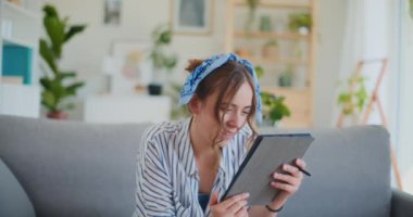 Odaklanmış ve üretken bir kadın, dijital tabletini kullanarak oturma odasının rahatlığında üretken bir atmosfer yaratıyor.