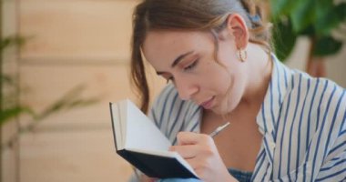 Kanepede oturan, notlar yazarken hayal kuran bir kadının yakın çekimi.