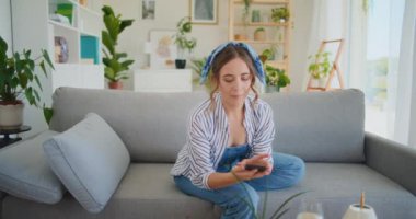 Neşeli bir gülümsemeyle, bir kadın akıllı telefonuyla başarılı bir online alışveriş yaptıktan sonra kanepede rahat bir şekilde uzanarak mutluluğun tadını çıkarıyor.