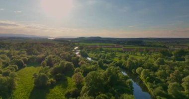 Bir kuş nehri ve günbatımını görür. Etrafında ormanlar ve yemyeşil doğa vardır.
