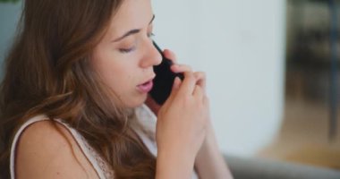 Evdeki koltukta oturan bir kadın cep telefonuyla konuşuyor.