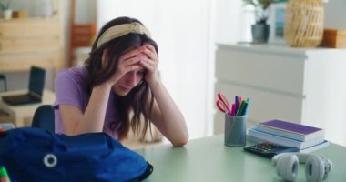 Genç bir öğrenci, okuldaki zorlu bir günün ardından üzgün bir şekilde masasında oturuyor.