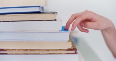 Genç bir öğrenci metaforik olarak eğitim ve kariyer hedeflerini simgeleyen bir yığın kitaba tırmanıyor.