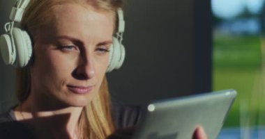 Dijital tablet kullanan ve müzik dinleyen düşüncelere dalmış düşünceli bir kadın.