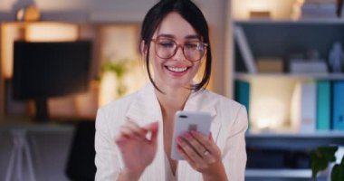 Mutlu bir iş kadını, akşam vakti ofisteki akıllı telefonuyla interneti karıştırıyor..