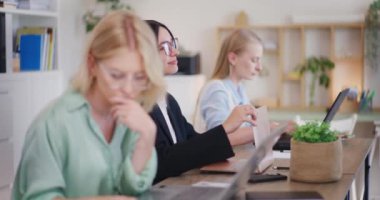 Kendine güveni olan bir kadın çalışanın laptopta çalışırken düşüncelere dalması, düşünceli ve düşünceli olması ve diğerlerinin yoğun çalışması..