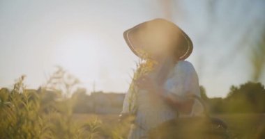 Mutlu kadın gün batımında kır çiçeği topluyor..