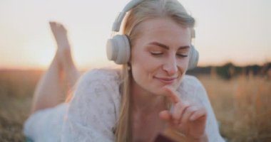 Mutlu kadın müzik dinliyor ve kitap okuyor altın bir günbatımında çayırda dinleniyor..