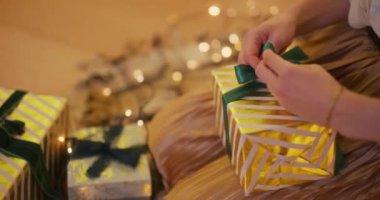 Bir kadının elleri, altın bir hediyeyi özenle sarıp sarmalar ve narin bir kurdele bağlar..