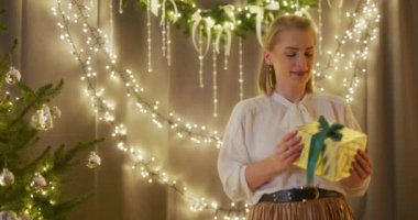 Mutlu bir kadın, parıldayan Noel ışıklarının sihirli parıltısıyla çevrili bir hediyeyi açar..