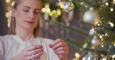 Bir kadın Noel büyüsünü bir ağacı süsleyerek yaratıyor, evde neşe ve coşku yayıyor..