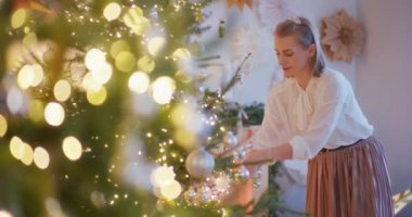 Bir kadın Noel ağacını neşeli bir şekilde süslüyor. Bayram ruhunu yayıyor..
