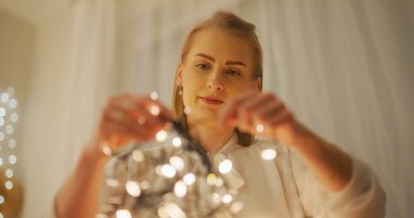 A woman prepares her home for Christmas, untangling lights and arranging festive decorations. clipart