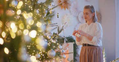 Bir kadın Noel ağacını neşeli bir şekilde süslüyor. Bayram ruhunu yayıyor..