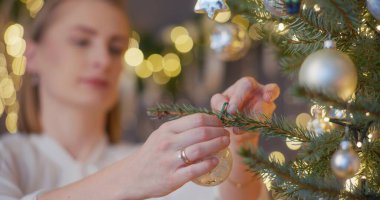 Bir kadın Noel büyüsünü bir ağacı süsleyerek yaratıyor, evde neşe ve coşku yayıyor..