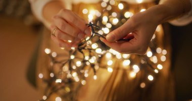 A close-up view of a woman untangling Christmas lights in the comfort of her home, preparing for the holidays. clipart