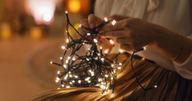 A woman untangles Christmas lights in a warm and cozy interior, creating a festive atmosphere at home. clipart