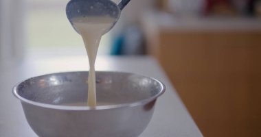 Bir kadın kepçeyle tavaya krep hamuru döker..