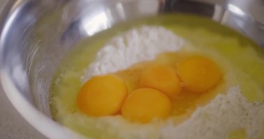 Birkaç çiğ yumurta bir kase un içinde hazır bekliyor, karıştırılmaya hazır..