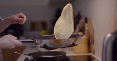 Bir kadın mutfakta kızartırken tavada krep çeviriyor..