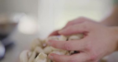 Kesilmiş mantarları mutfaktaki bir kaseye aktaran ellerin detaylı görüntüsü..