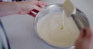 Bir kadın krep hamuru yoğunluğunu kontrol etmek için plastik spatula kullanır..