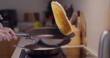 Bir kadın mutfakta kahvaltı hazırlarken tavaya krep atıyor..