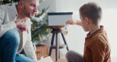 Bir baba ve oğlu ağaçlara renkli bir Noel mücevheri asar ve birlikte neşeli anılar yaratırlar..