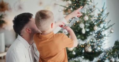 Baba ve oğul mutlu bir şekilde Noel ağacını süsler, neşeli anılar yaratırlar.