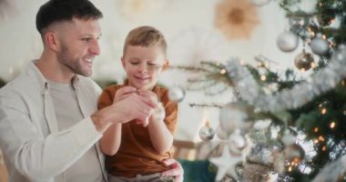 Bir baba ve küçük oğlu Noel ağacını süsleyerek şenlik sezonuna hazırlanıyorlar.